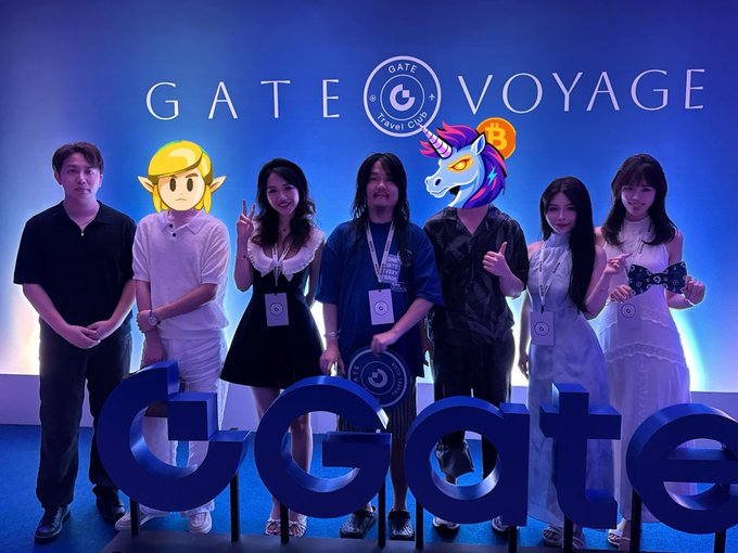 Six people pose at a 'GATE VOYAGE Travel Club' event in front of a blue backdrop with a unicorn mascot, standing behind large 'Gate' letters.