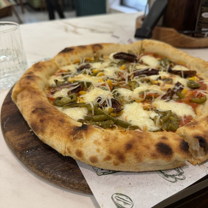 A rustic pizza topped with cheese, green peppers, corn, and other vegetables served on a wooden board.