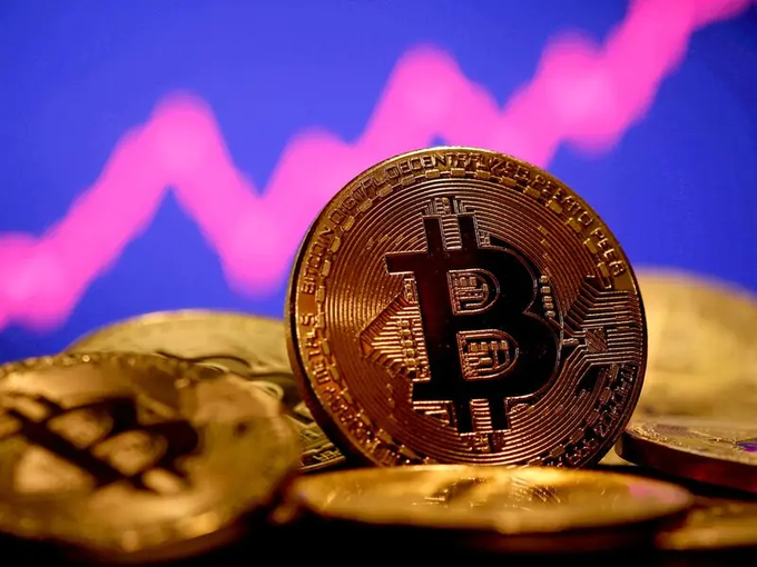 A gold-colored Bitcoin coin featuring the "₿" symbol stands prominently in focus, with additional coins scattered in the foreground and a blurred pink and blue chart line trending upward in the background. The image reinforces the post's reference to Bitcoin's historic $126,198 all-time high, symbolizing the cryptocurrency's dramatic price ascent.