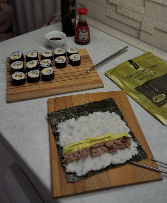 Sushi rolls in progress are laid out on wooden boards alongside a package labeled "YAKI SUSHI NORI GOLD Pkg" and bottles of soy sauce. The "Smash or Pass?" caption invites viewers to judge the homemade-looking rolls featuring fillings of tuna and avocado, with the answer clearly being a smash given the careful presentation and quality ingredients.