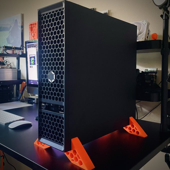 A black workstation tower with a hexagonal mesh front panel sits elevated on bright orange 3D-printed honeycomb feet on a desk, with the "LEAP" branding visible on the front. The post references selling this same Q-model PC with 10 months of remaining warranty, and the orange stands shown appear to be the custom 3D-printed accessory being discussed.