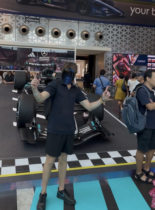 A person wearing a Darth Vader mask poses with peace signs in front of a Mercedes-AMG Petronas Formula 1 car display.