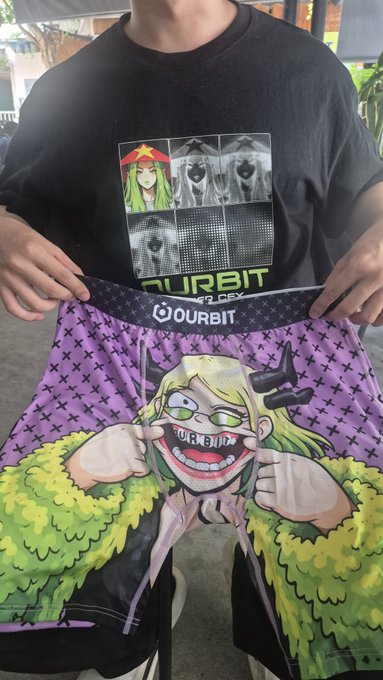 A person holds up a purple '$OURBIT' branded garment or shorts featuring a colorful cartoon character print, while wearing a black 'OURBIT' t-shirt.