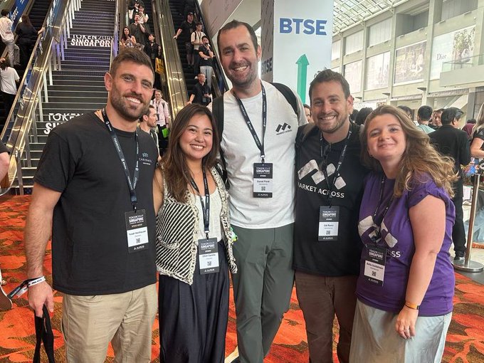 Five people wearing Singapore Token2049 conference lanyards pose together at the event, with a BTSE branded banner and escalator visible in the background.