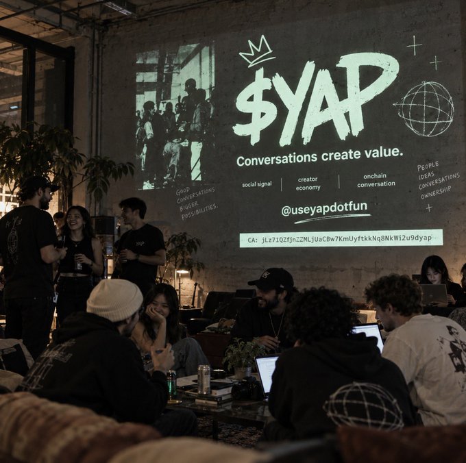 A dimly lit event space features a projected presentation for '$YAP: Conversations create value' with the handle @useyapdotfun and a crypto wallet address, while attendees socialize and work on laptops.