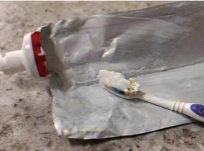 The image shows a toothbrush with some toothpaste on it, placed on top of a piece of foil or aluminum foil that has been cut open. The foil appears to be dirty, possibly due to being used for wrapping food items. The background is blurred, but there are words visible in the image which seem to be related to cryptocurrency and the post about it.