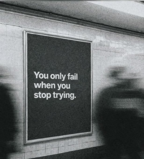 A black and white photograph of an advertisement poster on a tiled wall, likely in a subway station, featuring the motivational quote "You only fail when you stop trying." with a blurred figure walking past.