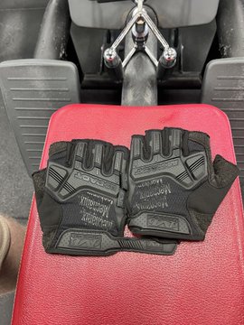 A pair of black Mechanix M-Pact tactical gloves resting on the red leather seat of a motorcycle or ATV.