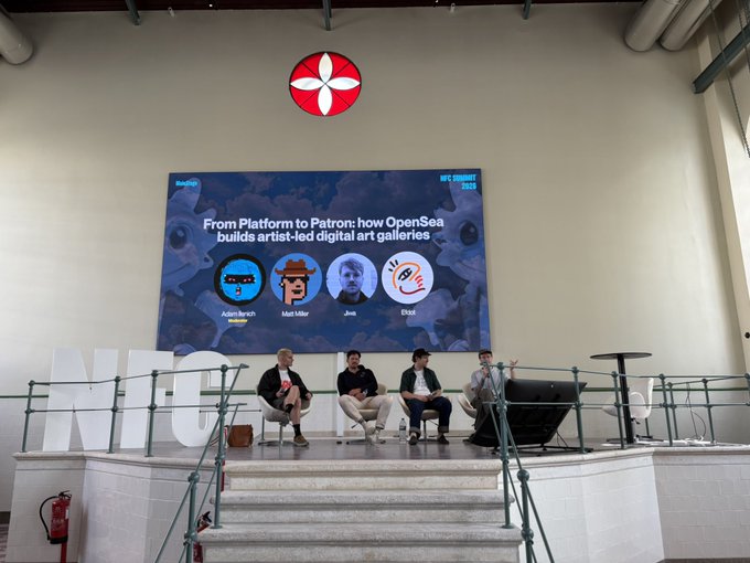 The image shows a group of four people sitting around a table, with three men and one woman. They are all facing towards a large screen that displays an advertisement for OpenSea. The screen also features a red circle with a white flower on top. The text in the image reads "From Platform to Peer-to-Peer how OpenSea handled digital art collections and artist activations, platform direction, and the collector communities keeping crypto art alive".