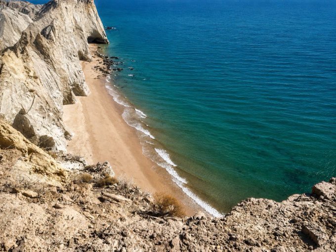 A scenic coastal view looking down from rocky cliffs onto a small sandy beach meeting turquoise ocean waters.