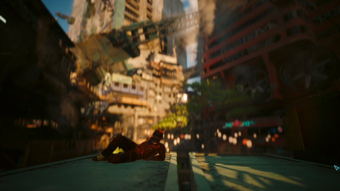 A scene from a video game featuring a character with red robotic arms lying on a blue-tiled rooftop, looking out over a detailed, futuristic, cluttered cityscape.