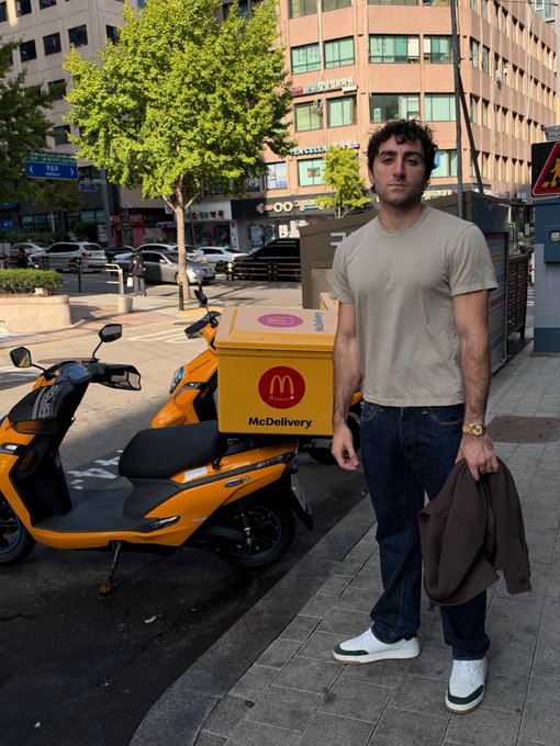 A man stands on a Seoul sidewalk beside a bright yellow McDelivery scooter, heading to speak at the @Ondo event.