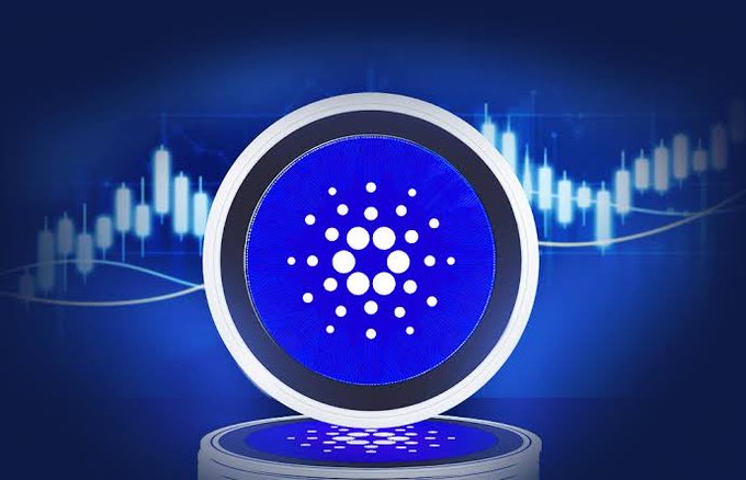 A digital illustration of a glowing blue circular token or coin featuring the Cardano (ADA) logo, displayed on a pedestal with candlestick charts in the background.