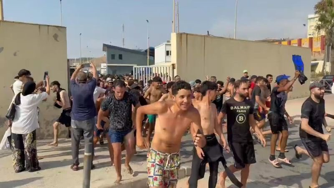 A large crowd of people, many shirtless, run through a street gate, with one man prominently wearing a "BALMAIN PARIS" t-shirt, suggesting a chaotic scene often seen in meme coin or pump-and-dump promotions. The caption ties the image to a post mocking Pumpfun tokens, implying that despite efforts to "cleanse" such schemes, the frenzied crypto culture continues to attract crowds chasing the next viral token.