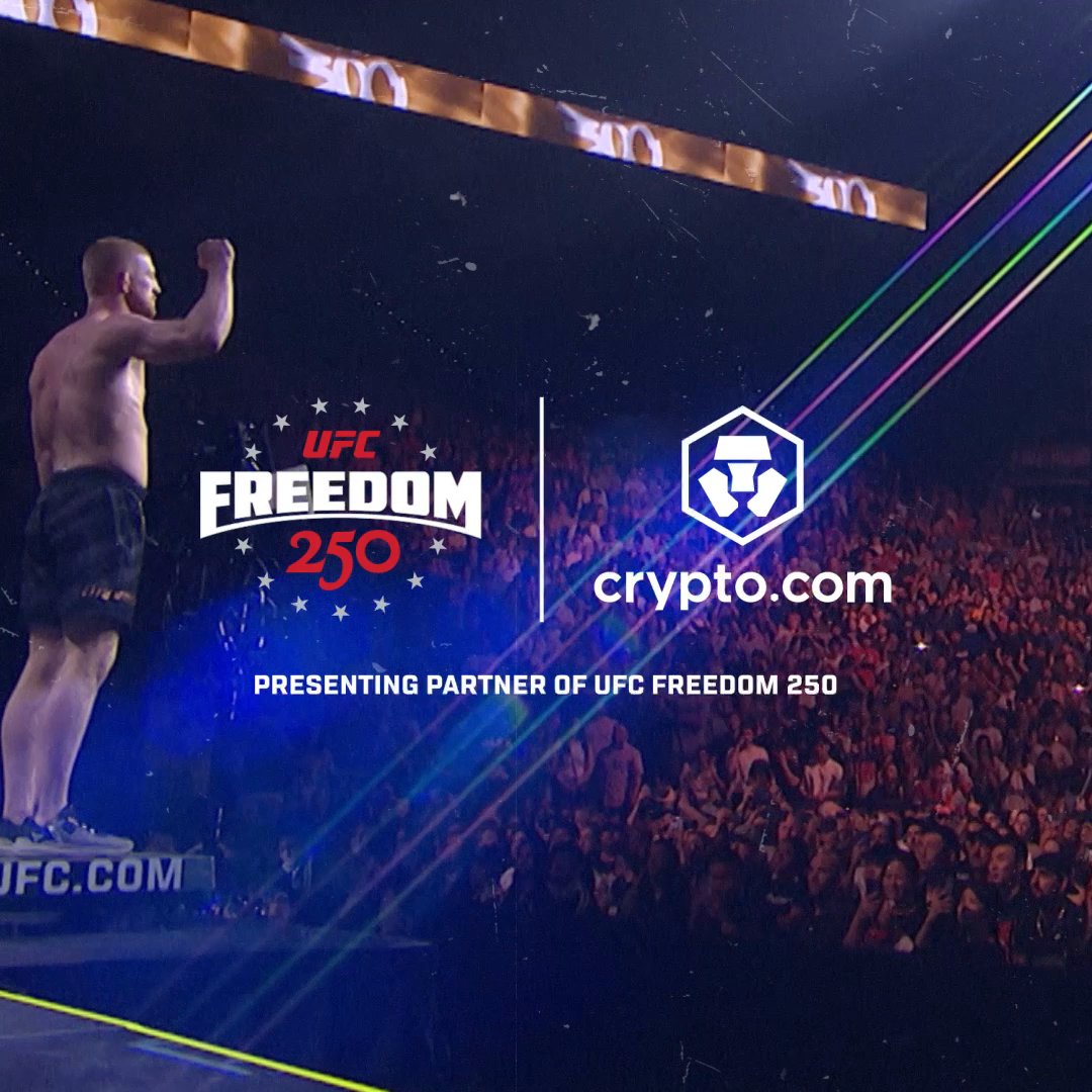The image features a man standing on stage at a UFC event, with a crowd of people watching him. The background shows a large screen displaying the words "UFC Freedom 250" along with a logo for a cryptocurrency called "crypto.com". The text also mentions that the fighter is presenting his partner in this event.