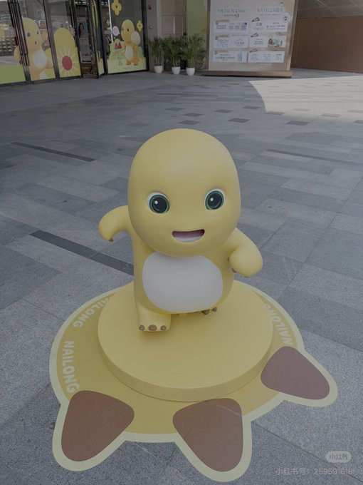 A yellow dinosaur-like mascot statue on a circular yellow pedestal with 'NAILONG' written on it, displayed outside a shop.