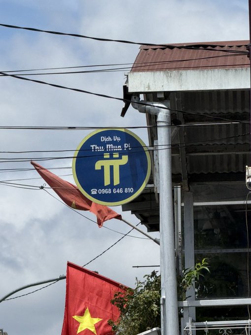 A blue and yellow circular sign reading 'Dịch Vụ Thu Mua Đồ' (second-hand goods buying service) with the phone number 0968 646 810, mounted on a pole in Vietnam with a Vietnamese flag and red flag visible below.