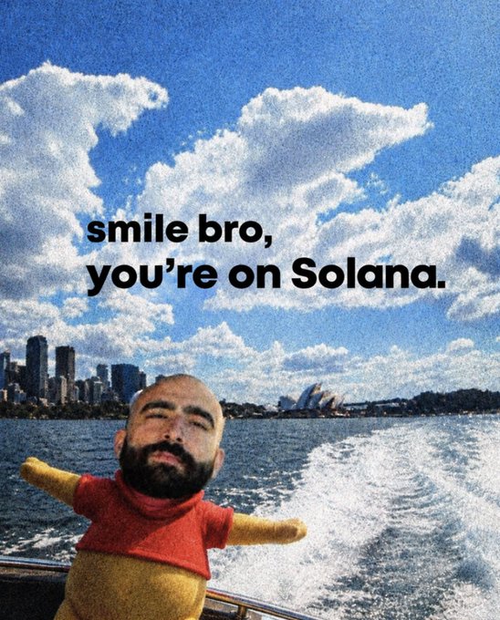A meme-style image shows a bearded man's face photoshopped onto a small figure in a red shirt standing on a boat wake, with the text "smile bro, you're on Solana." overlaid against a backdrop of a coastal city skyline with the Sydney Opera House.