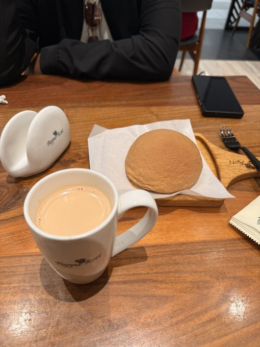 A cup of chai sits beside a signature Pappa Roti bun on a wooden table, with a branded Pappa Roti cup and saucer nearby, capturing the Dubai café experience mentioned in the post.