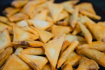 A close-up photo of a pile of golden-brown fried triangular pastries, likely samosas, with crispy folded edges.