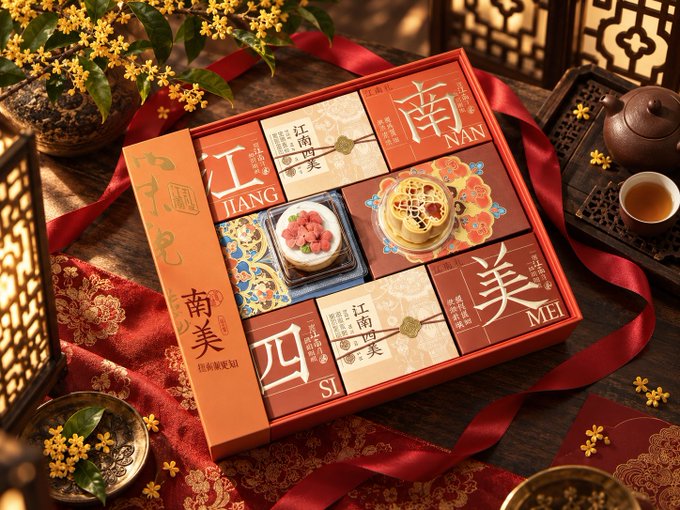 An ornate gift box of traditional Chinese pastries with compartments labeled with Chinese characters meaning 'Jiang', 'Nan', 'Mei', and 'Si', displayed with osmanthus flowers, red ribbons, and a teapot.