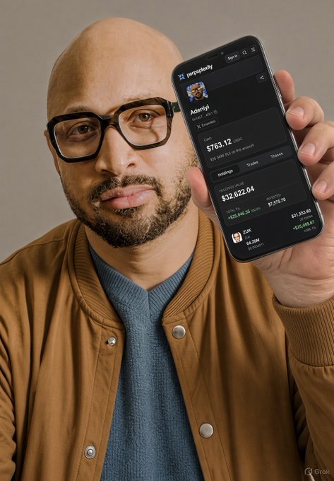 A bald man with glasses and a beard wearing a brown jacket, holding up a smartphone displaying a financial portfolio app showing an account value of $763.12 and holdings of $32,622.04.