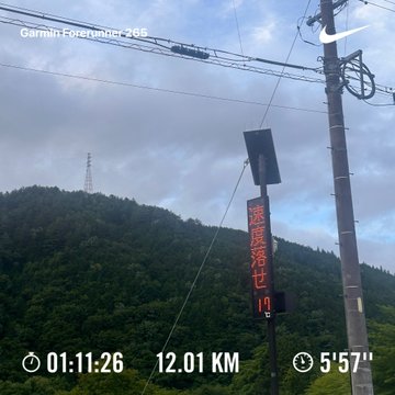 A first-person view from a Garmin Forerunner 265 cycling computer showing 12.01 km traveled in 5'57" at 01:11:26, with power lines and a Chinese road sign indicating a descent ahead.