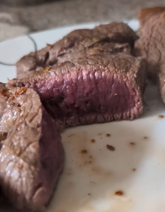 Close-up photo of sliced cooked beef steak showing a pink, medium-rare interior with a browned seared exterior, served on a white plate.