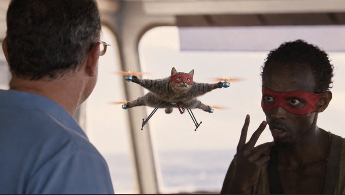A humorous edited movie scene shows a man in a red mask looking in shock at a drone with a cat's body and red mask hovering in the air.