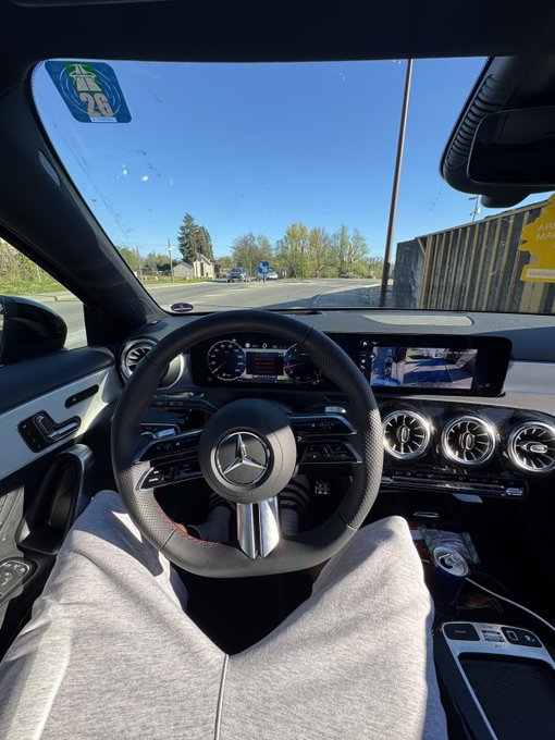 A first-person POV photo taken from the driver's seat of a Mercedes-Benz, showing the steering wheel and dashboard on a sunny day.