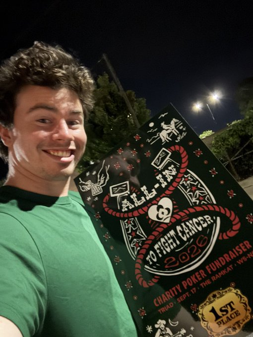 A smiling young man in a green t-shirt poses at night with a poster for the 'All-In Poker to Fight Cancer 2020' charity fundraiser, which won 1st place.