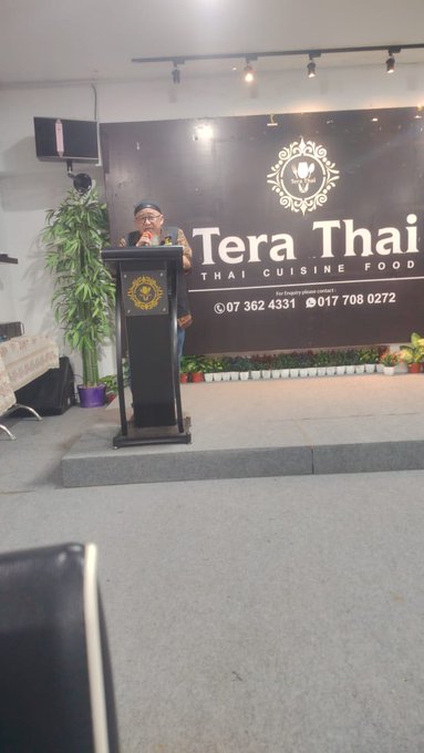 A speaker presents at a podium in front of a "Tera Thai Thai Cuisine Food" banner displaying contact numbers 07 362 4331 and 017 708 0272, likely addressing the Pi Network community members tagged in the post during a PiCoreTeam gathering in Malaysia.