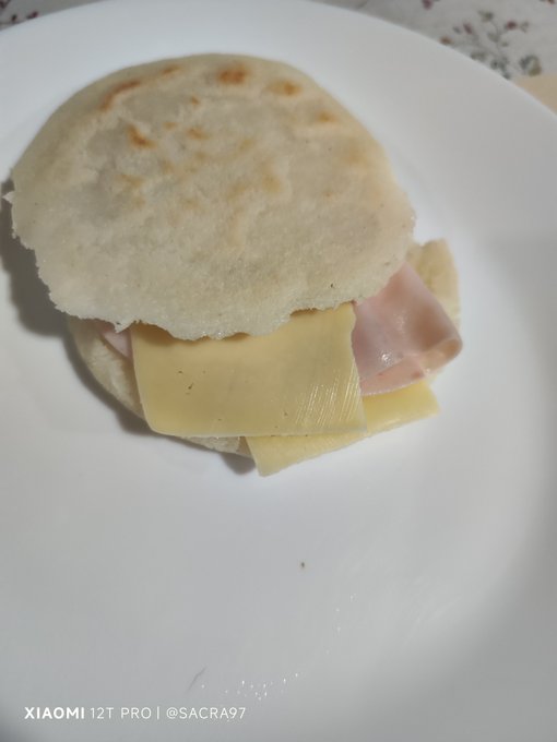 A simple sandwich made with a round flatbread, sliced ham, and yellow cheese sits on a white plate, with a watermark reading 'XIAOMI 12T PRO | @SACRA97' visible.