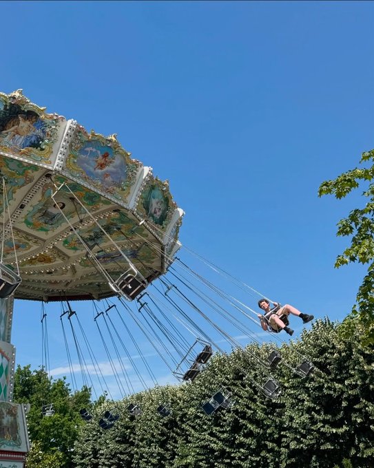 A colorful swing carousel ride in motion against a clear blue sky, with riders suspended by chains swinging outward from the decorated canopy.
