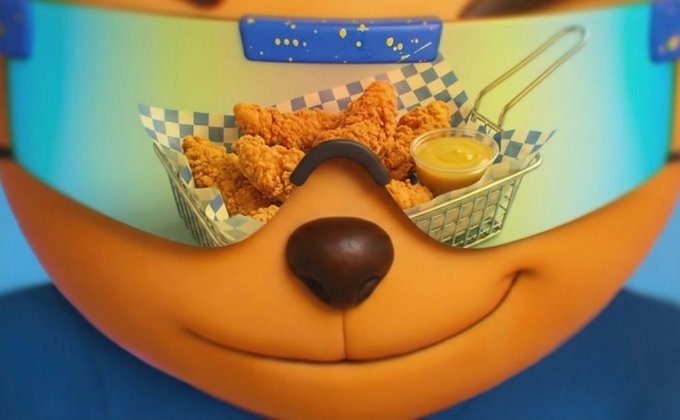 A novelty serving basket shaped like an orange dog's face holds fried chicken tenders with a small cup of dipping sauce.