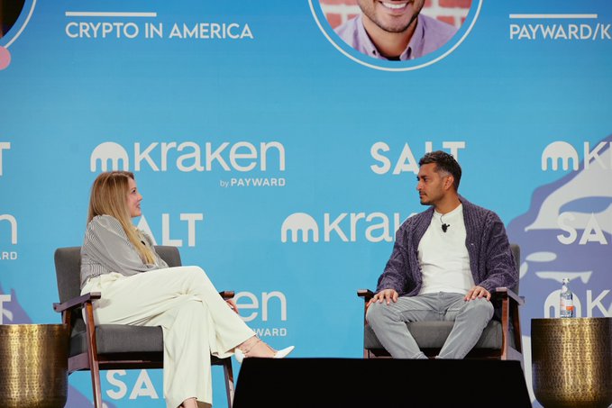 Arjun Sethi, co-CEO of Kraken/Payward, sits on stage in a fireside chat with Eleanor Terrett at the 2026 Wyoming Blockchain Symposium, against a backdrop featuring the event's "Crypto in America" branding alongside the Kraken by Payward and Salt logos.