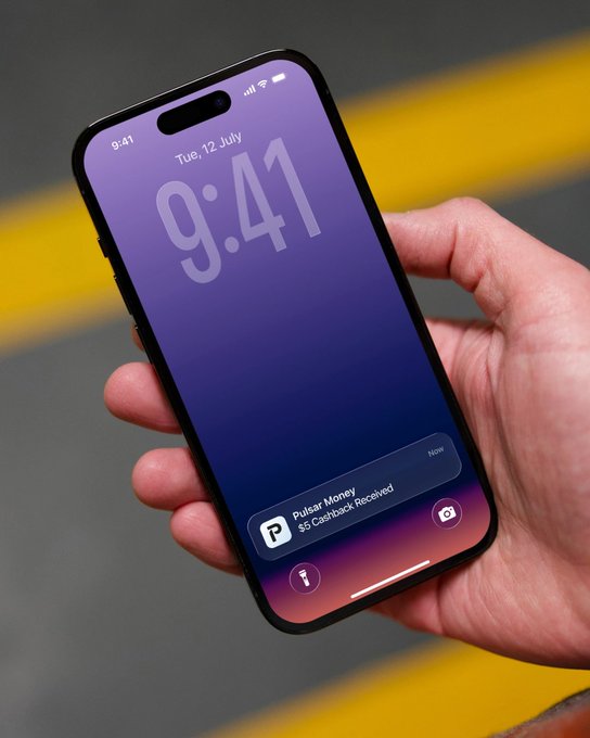 A hand holds an iPhone displaying the lock screen with time '9:41' and date 'Tue, 12 July', along with a notification reading 'Pulsaar Money $5 Cashback Received'.