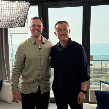 Two men pose together smiling in a modern high-rise setting with ocean views through floor-to-ceiling windows, capturing the moment from the launch of The Block's new daily show featuring Binance founder Changpeng Zhao (CZ) as the inaugural guest.