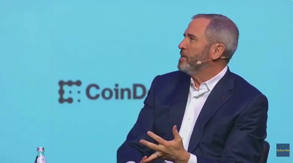 The image features an older man dressed in a suit, sitting behind a table with his hands together as if deep in thought or conversation. The backdrop consists of blue text, possibly related to digital asset management platforms such as Bitcoin, which suggests that this might be a discussion on the topic of cryptocurrency and off-chain transactions. One line of text stands out: "RIPPLE CEO: $4 TRILLION OF TREASURY FLOWS COULD MOVE ON-CHAIN WITHIN 5 YEARS @bgarlinghouse predicts roughly 30% of the $13 trillion treasury management market will move on-chain". This implies that there is a potential future trend where off-chain transactions could become more prevalent due to significant amounts being transferred within five years. The image captures this moment of thought and contemplation in the context of financial discussions, with an older man providing insights into these developments.