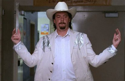 The image features an actor dressed in a white cowboy hat, jacket, and shirt standing in front of a building with his arms outstretched as if he's about to do something or make a gesture. The surrounding area appears to be a hallway, which is part of a larger room that seems to be a school or office space. There are also two handbags visible in the scene, one near the actor and another further away from him.