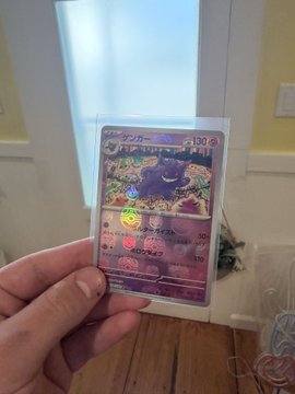 A hand holding a Japanese Pokémon card featuring Snubbull in a protective sleeve, with text indicating '130' HP.
