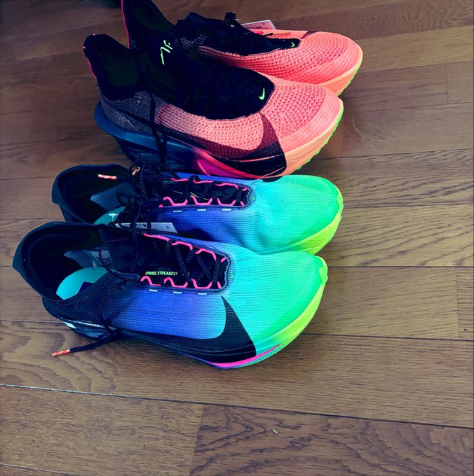 Two pairs of brightly colored Nike athletic shoes resting on a wooden floor; the top pair is pink and black, while the bottom pair is blue and green with the text 'NIKE STREAKFLY'.