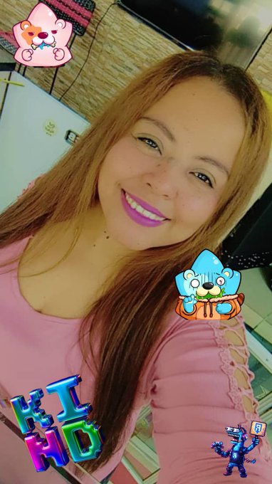 A selfie of a smiling woman with blonde hair wearing a pink Hello Kitty top, decorated with cute cartoon stickers and filters.