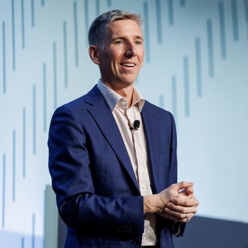 Bitwise CIO Matt Hougan speaking at a conference, smiling while addressing an audience about his bullish outlook on crypto valuations, noting that revenue-generating protocols like DeFi and Layer 1s appear undervalued as they return capital to token holders.