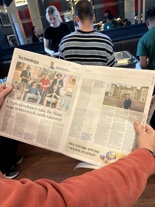 The image shows someone in an orange sweatshirt reading a newspaper with a Technology section article headlined "Crypto developers take the Slane stage in two-week castle takeover," alongside photos of the team in front of Slane Castle—visually confirming the "making literal headlines" claim about crypto's presence in Ireland.