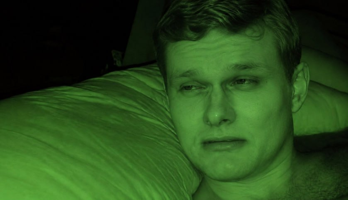 A close-up of a man resting his head on a pillow, with the entire scene tinted in a green night-vision filter.