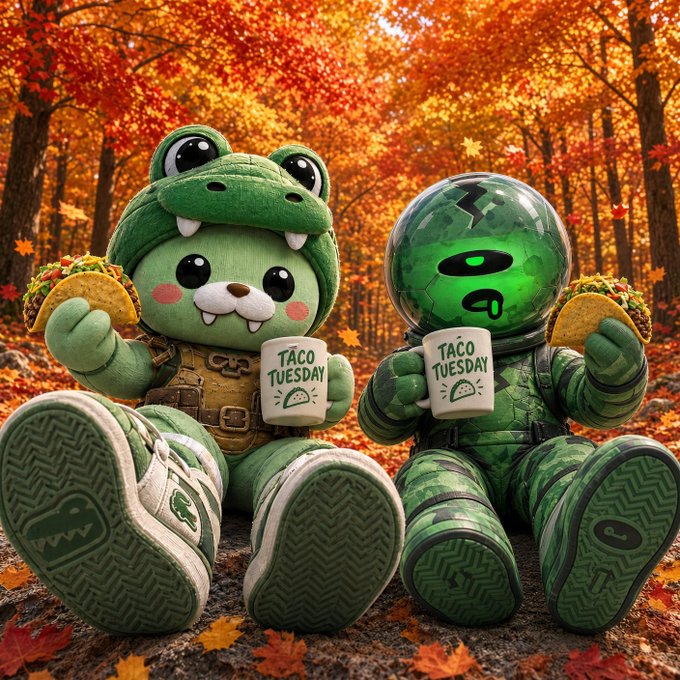 Two green plush characters—one a frog in tactical gear, the other a spaceman—sit against a vibrant autumn backdrop, each holding a taco and a mug labeled "TACO TUESDAY." The cozy fall vibes and playful taco theme perfectly match the post's cheerful "Taco Tuesday" energy and gratitude-filled message.
