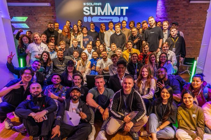 A large group photo of attendees at the 'SOLANA SUMMIT Germany' event posing together under a blue and purple illuminated banner.
