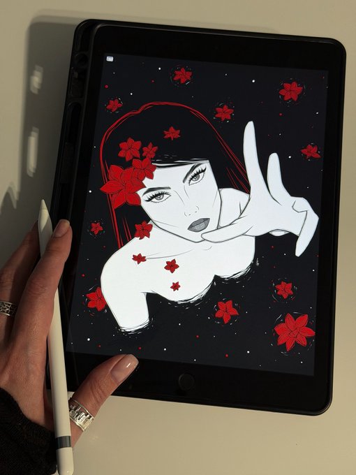 A hand adorned with rings holds a stylus while displaying a striking digital illustration on a tablet, featuring a stylized woman with red flowers scattered across a dark, starry background—likely showcasing the artist's recent NFT sale collaboration.