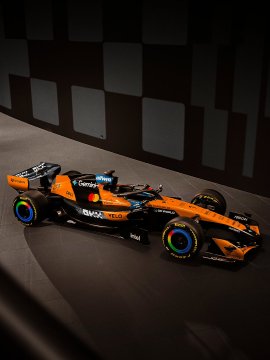 A sleek Formula 1 race car in orange and black livery with 'Chrome' and 'OKX' sponsor logos displayed against a checkered background.